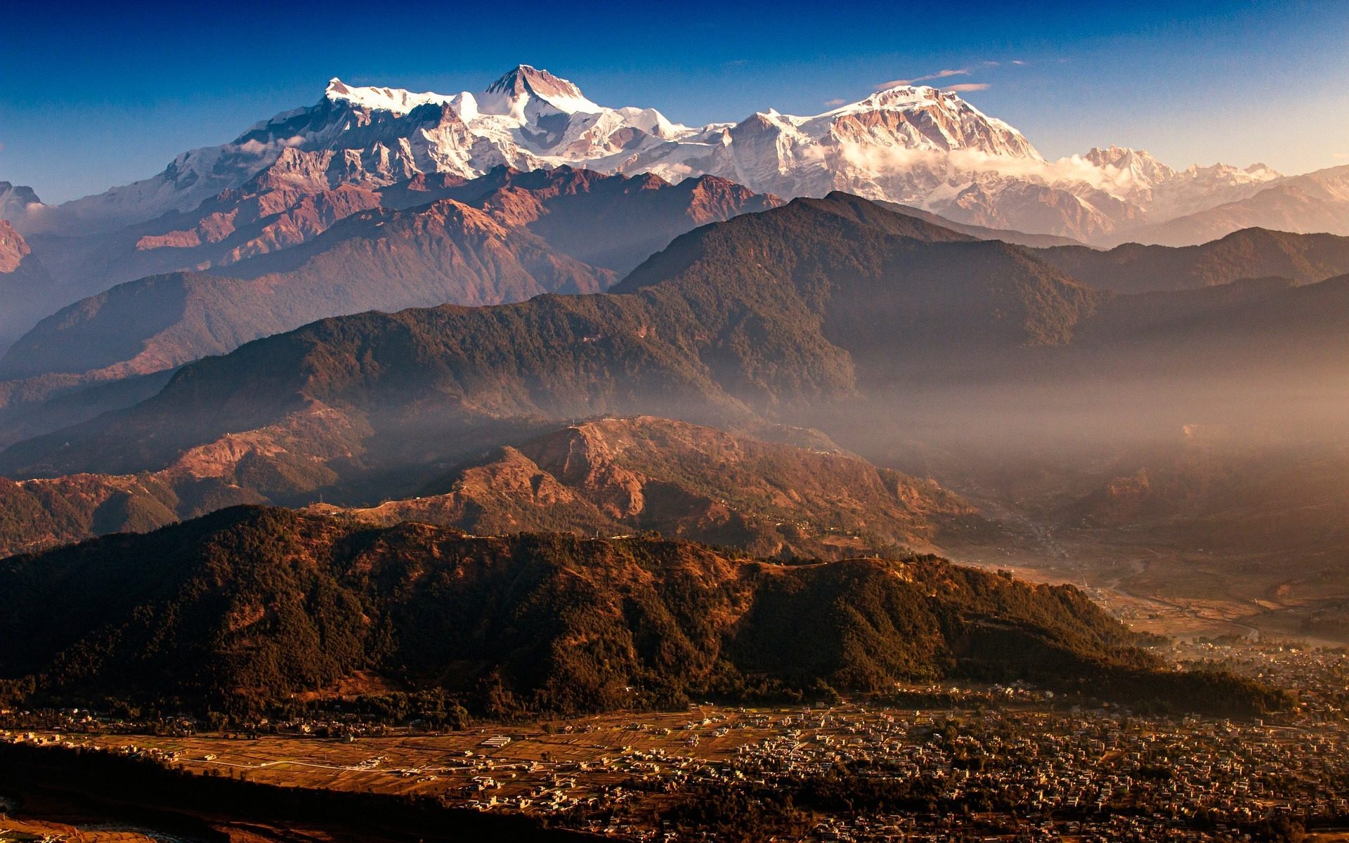 Layered Himalayan ridges under a clear sky with snow-capped peaks catching the light