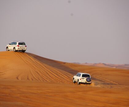 Two white 4x4 vehicles dune bashing on orange sand dunes during a Dubai desert safari