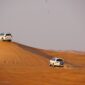 Two white 4x4 vehicles dune bashing on orange sand dunes during a Dubai desert safari