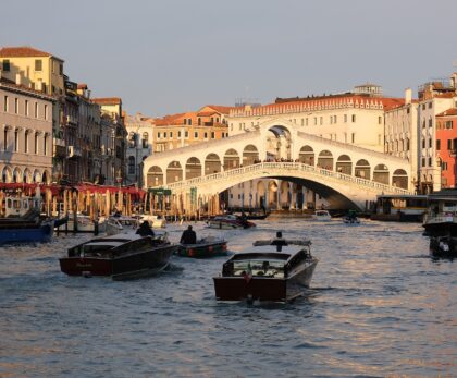 The Rialto Bridge over the Grand Canal in Venice at golden hour, with water taxis in the foreground