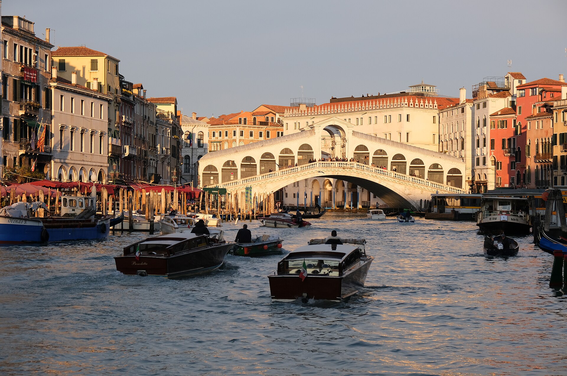 The Rialto Bridge over the Grand Canal in Venice at golden hour, with water taxis in the foreground